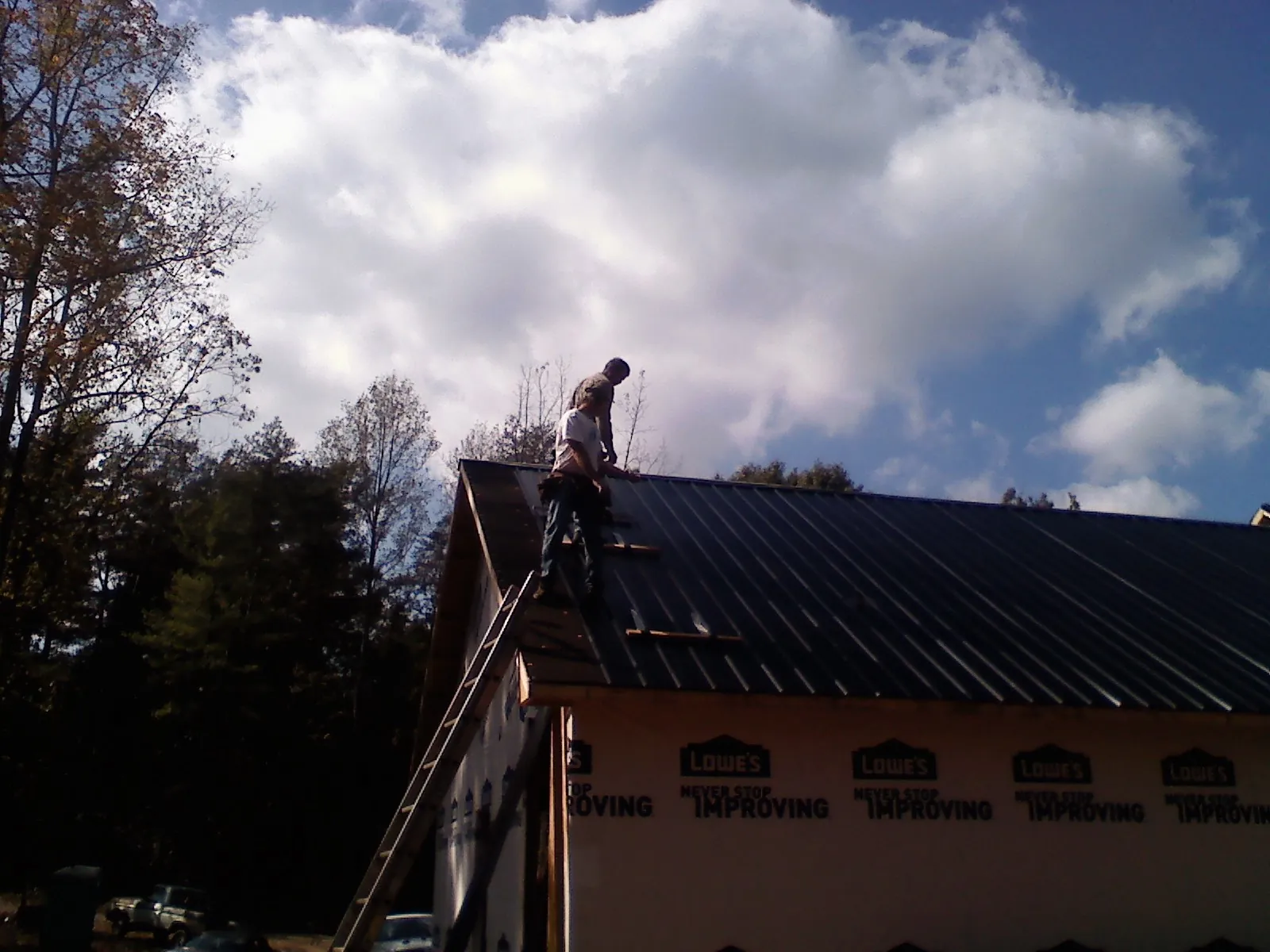 Roofer fastening dark metal panels high against a cloudy sky, from a Roof Inspection job in La Push